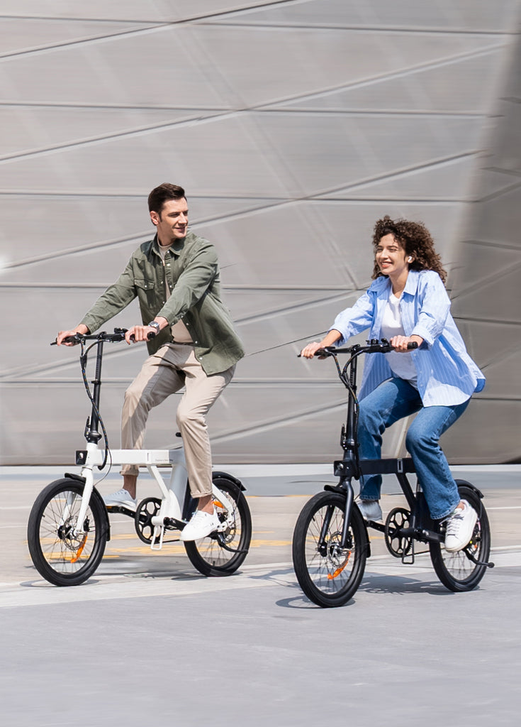 a man rides a white p20 and a woman rides a black engwe p20 electric commuter bike on the road